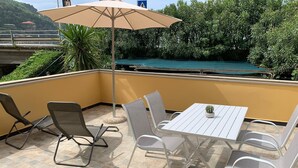 A patio with a table and chairs, a large umbrella, and a view of a pool and greenery.