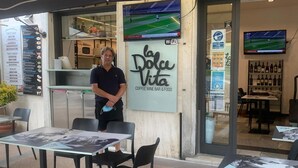 An outdoor seating area with tables and chairs, a menu board, and a sign for 'La Dolce Vita Coffee Wine Bar & Food'.