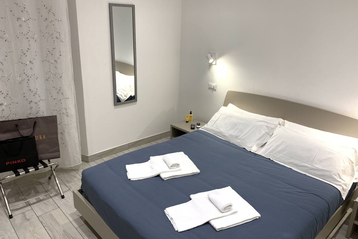 Una habitación de hotel con cama, mesita de noche, espejo y maleta.