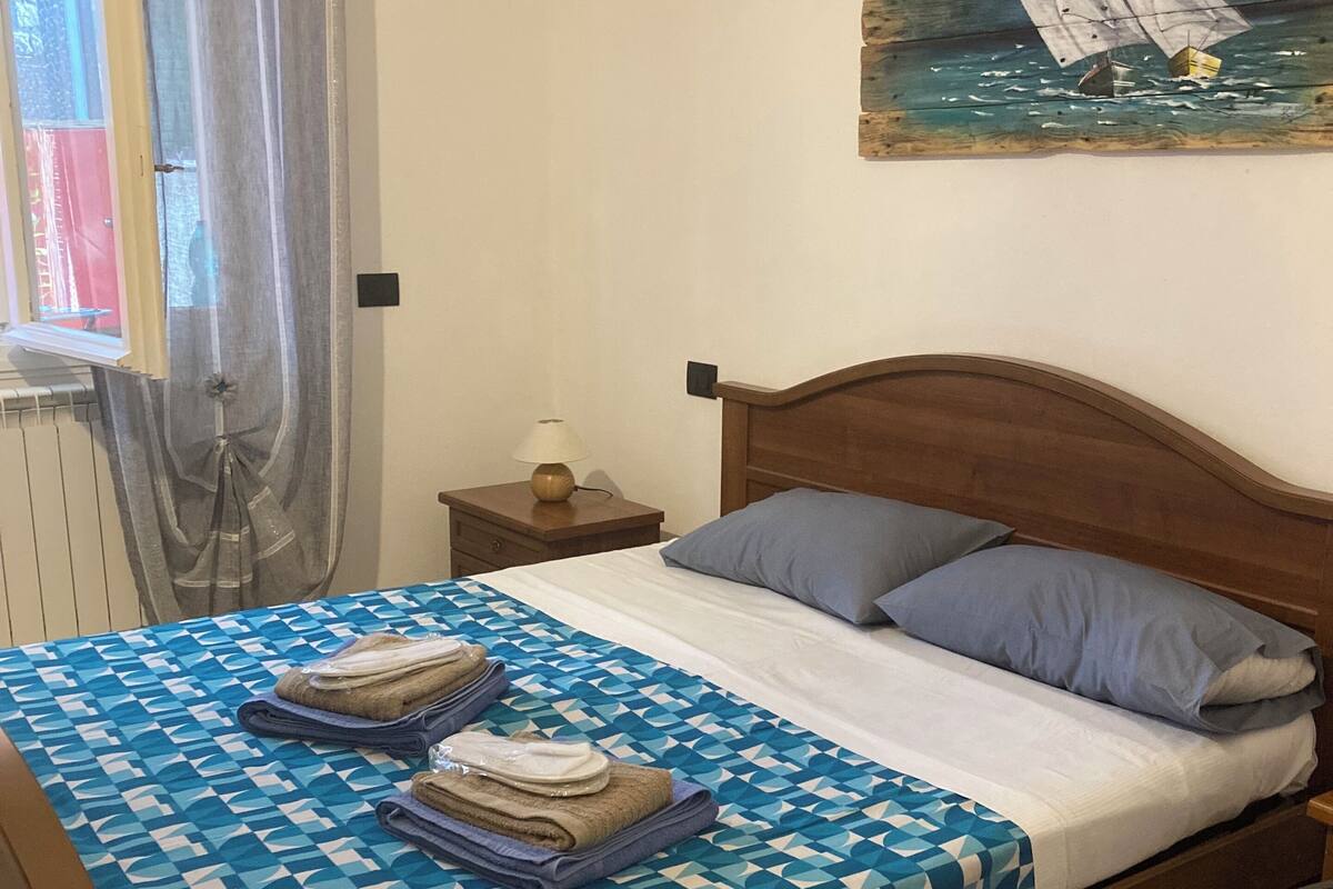 Un lit bien fait, avec une couvre-lit à motifs géométriques, une tête de lit en bois et un tableau représentant un voilier accroché au mur.