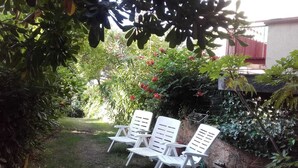 A garden with three white plastic chairs and a small lawn area. - Guest House Berzefi (Bergeggi)