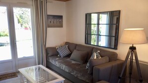 A living room with a sofa, a glass-top coffee table, a floor lamp, and a view of the outdoors through a window. - Renovated house Ile de Noirmoutier (L'Epine), in a quiet dead end, garden! (L'EPINE)