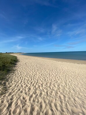 Une plage de sable où l’on peut voir des empreintes de pas menant à l’eau, sous un ciel bleu et dégagé.