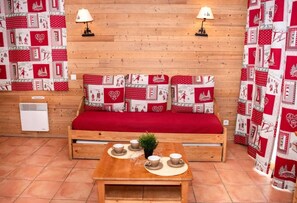 A cozy room with a wooden sofa, a small table with cups, and a red blanket.