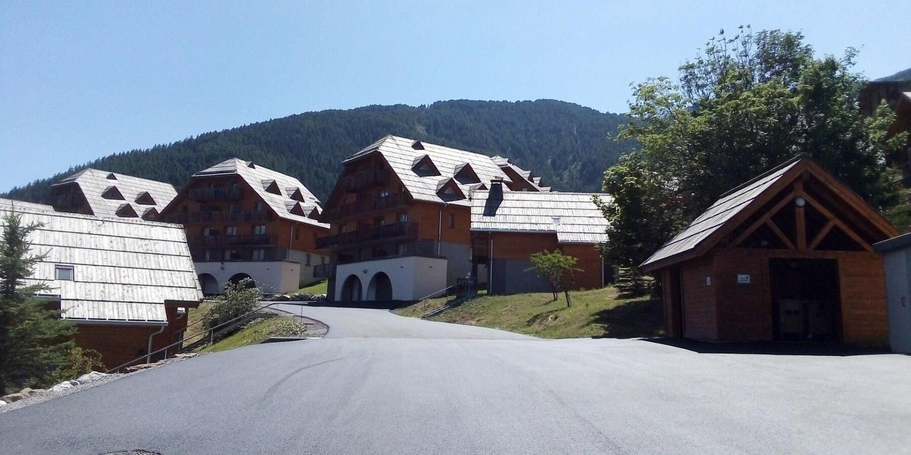 Reihenweise Chalets mit Satteldächern, eine zentrale Straße und eine Bergkulisse im Hintergrund.