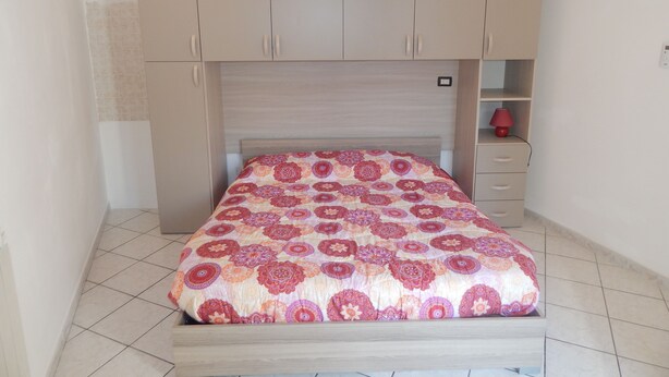 Quarto com cama, cabeceira de madeira, roupeiro embutido e mesa de cabeceira com abajur.