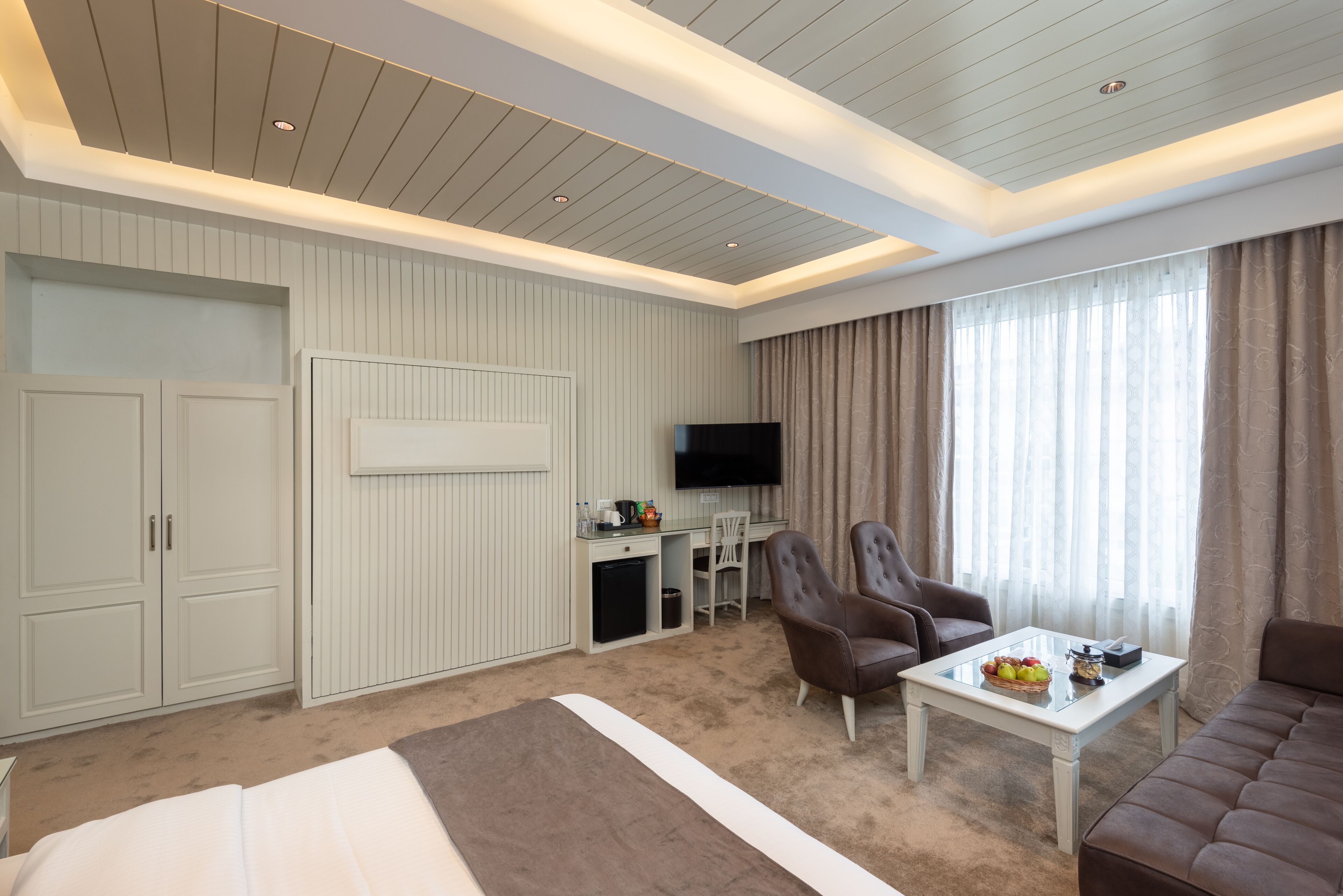 A hotel room with a bed, a seating area with a table and chairs, a TV, and a wardrobe.