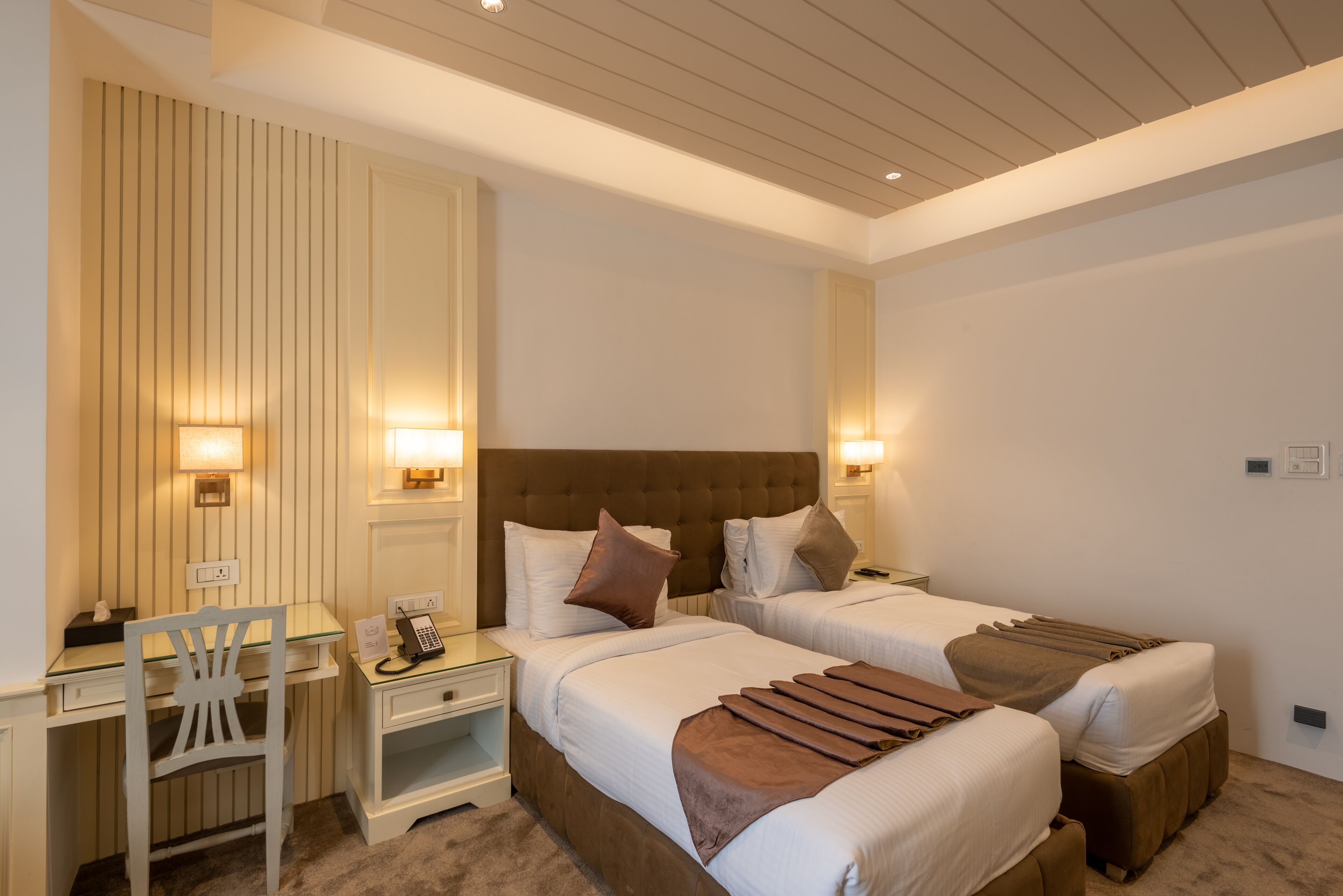 A hotel room with two beds, a desk, and a chair.