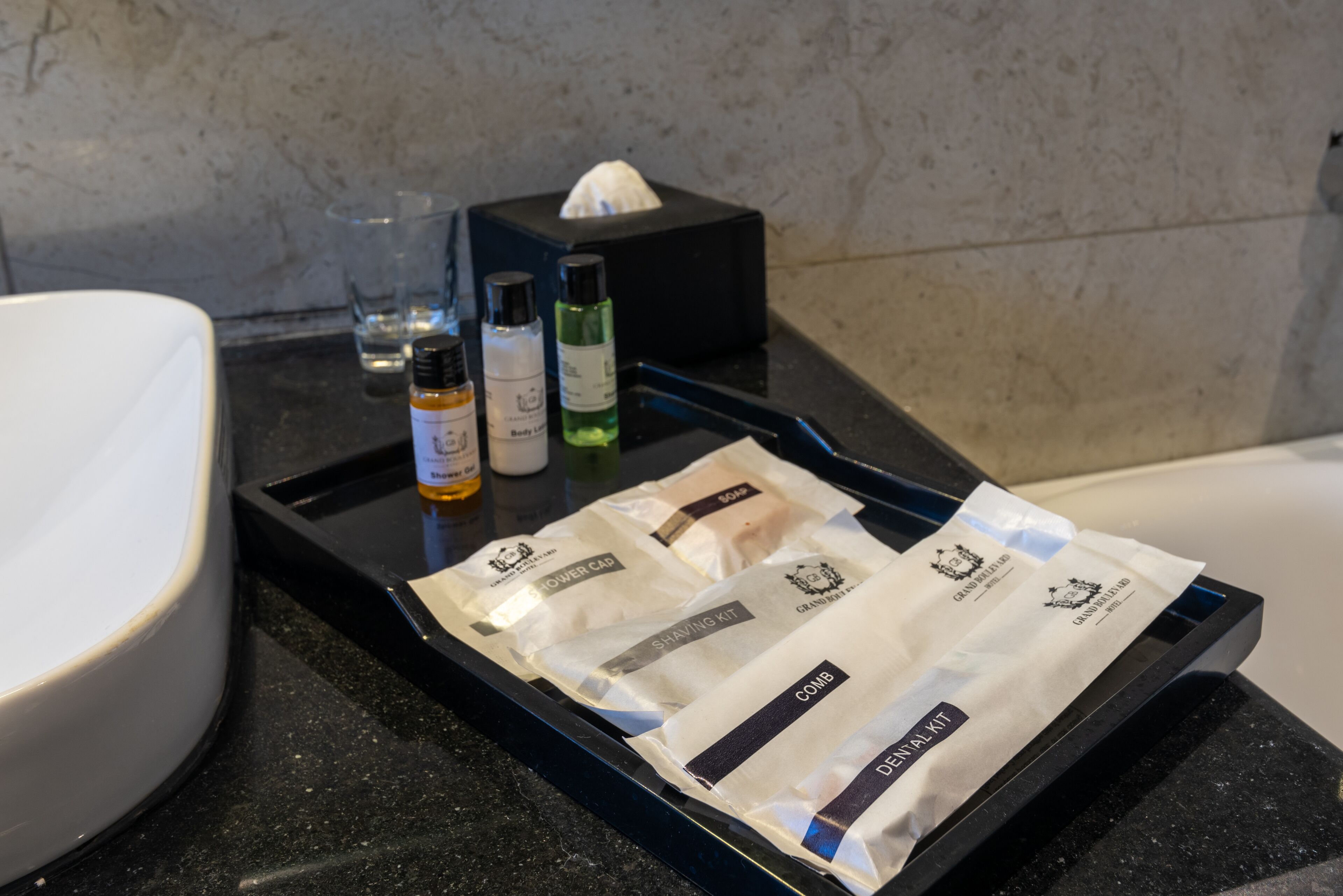 Una encimera de baño con un recipiente que contiene artículos de aseo, una caja de pañuelos y una botella de champú.
