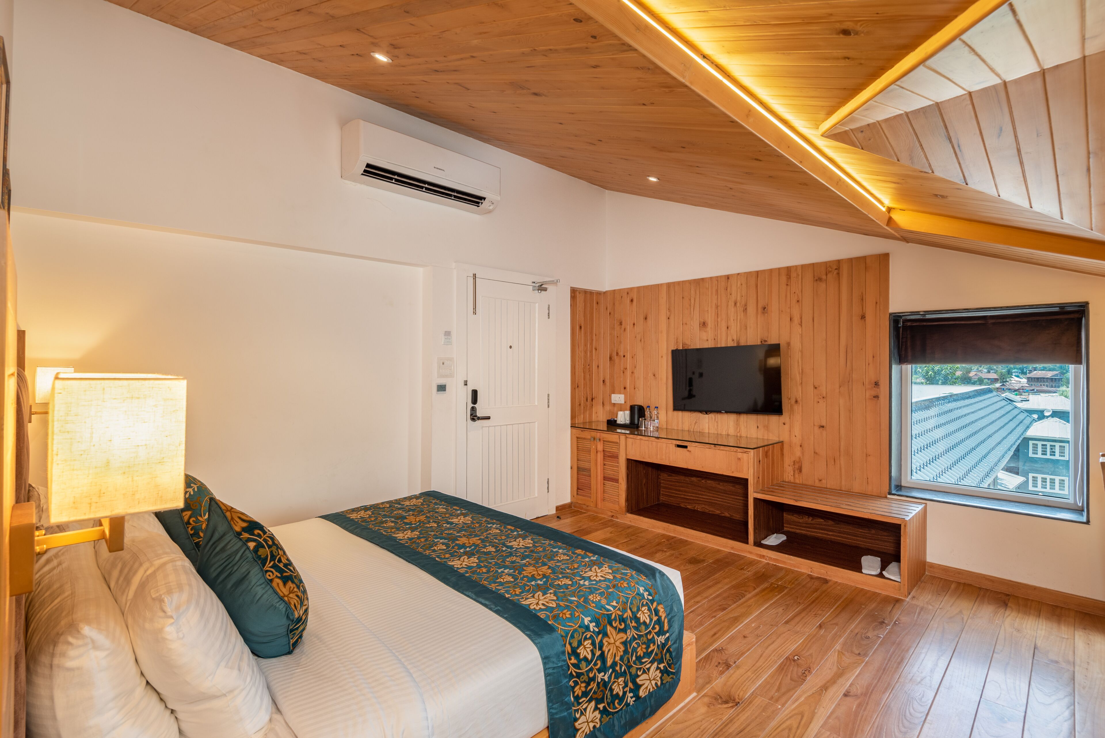 A bedroom with a bed, a TV, a window, and wooden paneling.
