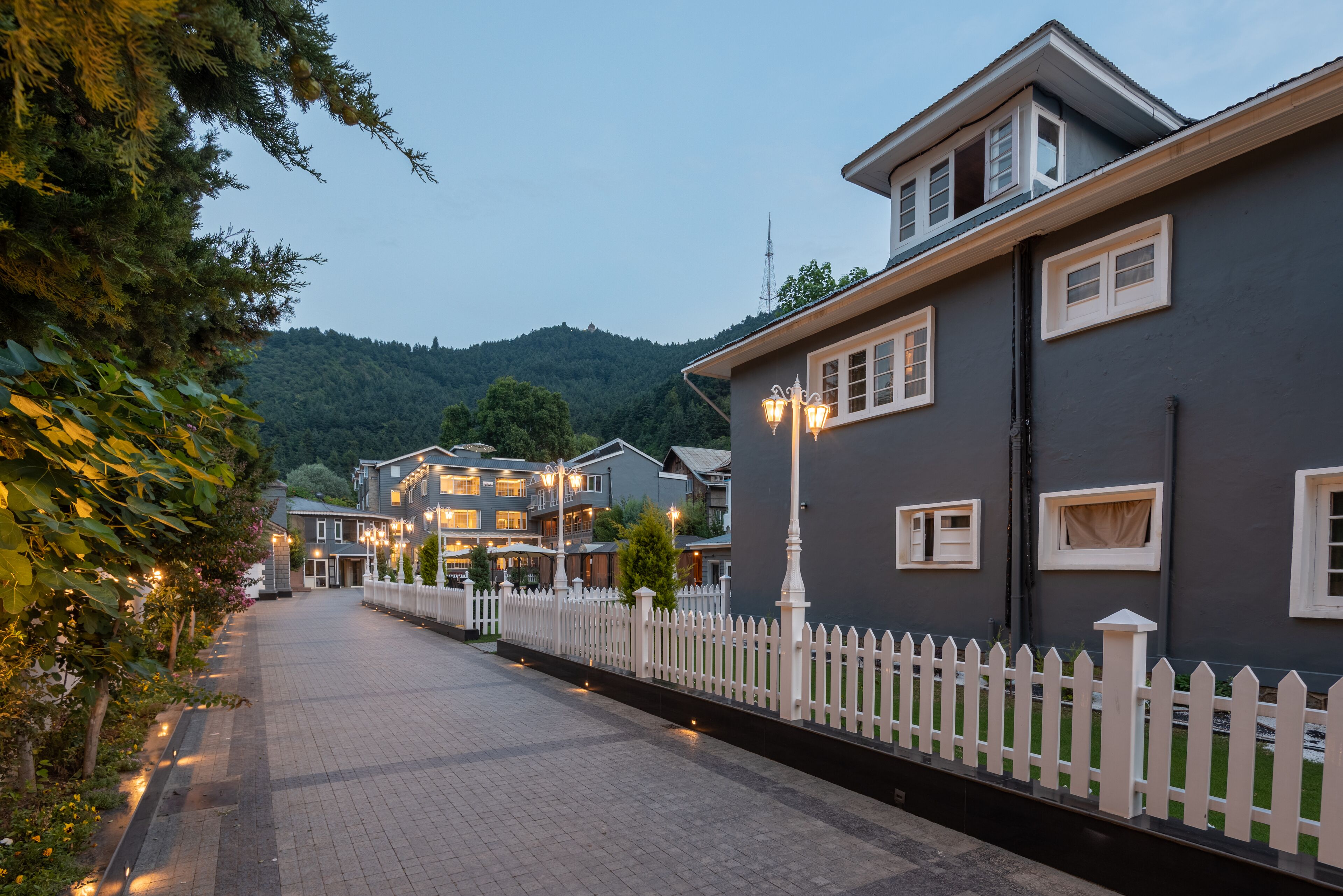 A street lined with multi-story buildings, a white picket fence, and a paved walkway.