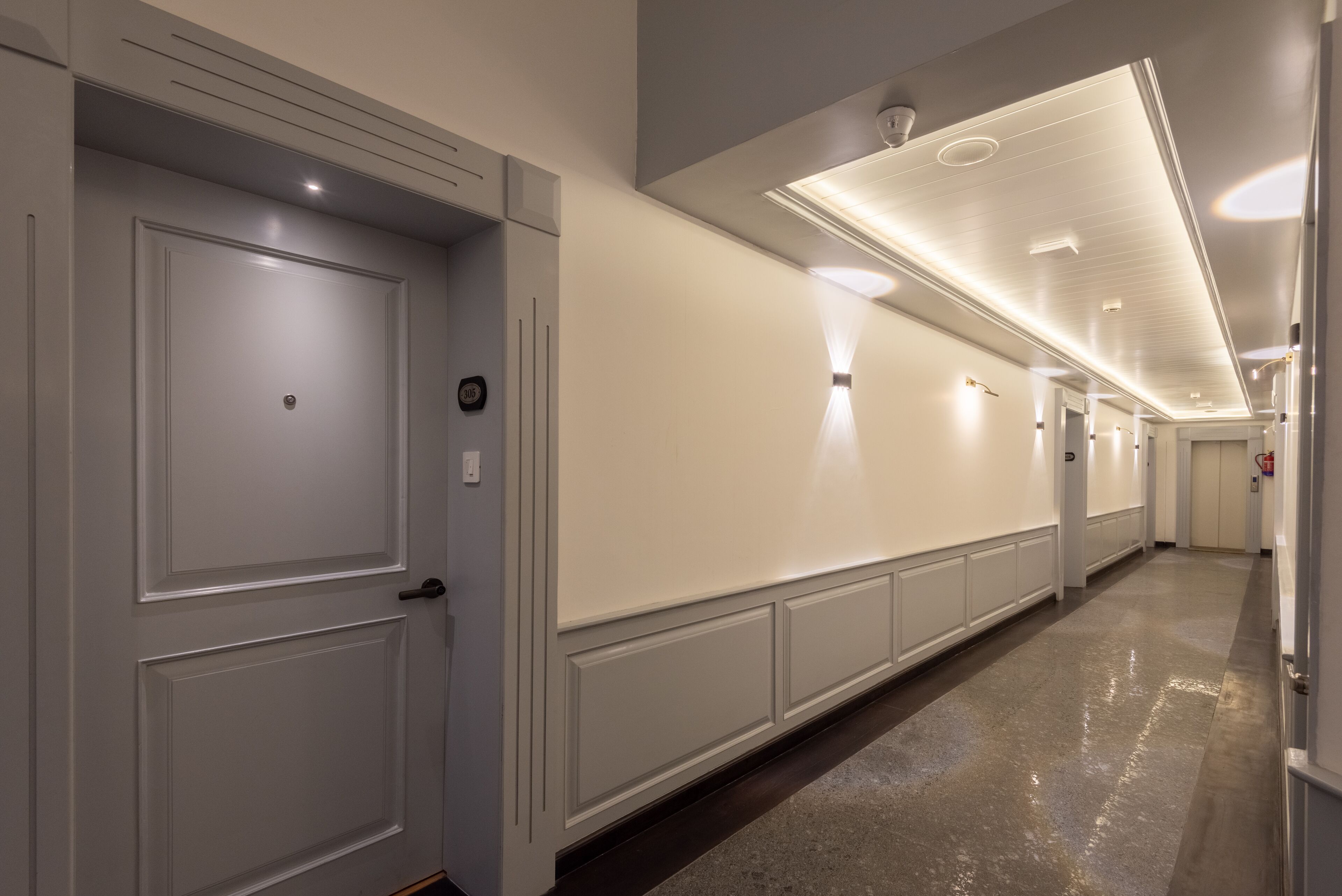 Corredor com paredes brancas, piso lustroso e iluminação embutida.