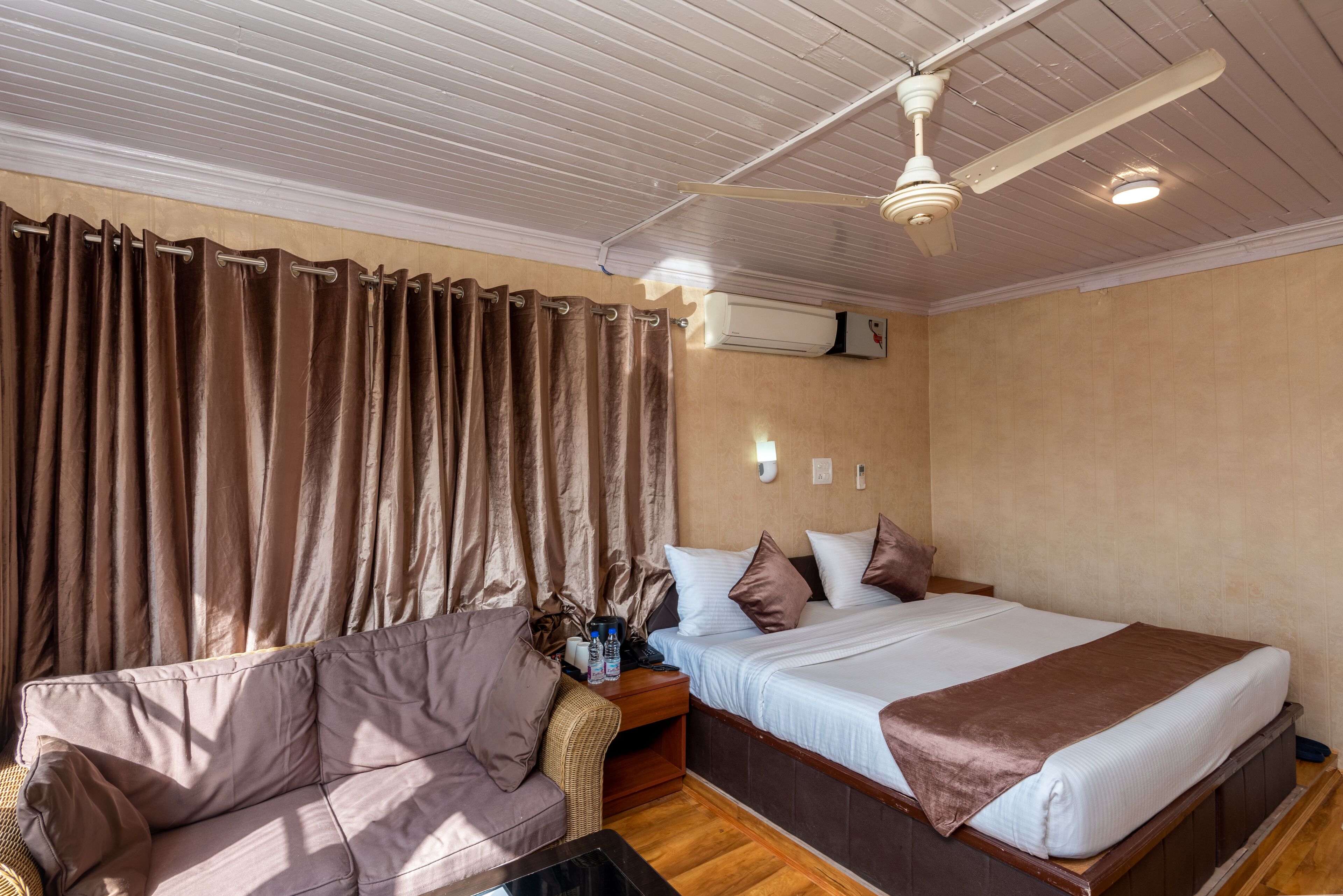 A bedroom with a bed, a sofa, an air conditioning unit, and a ceiling fan.