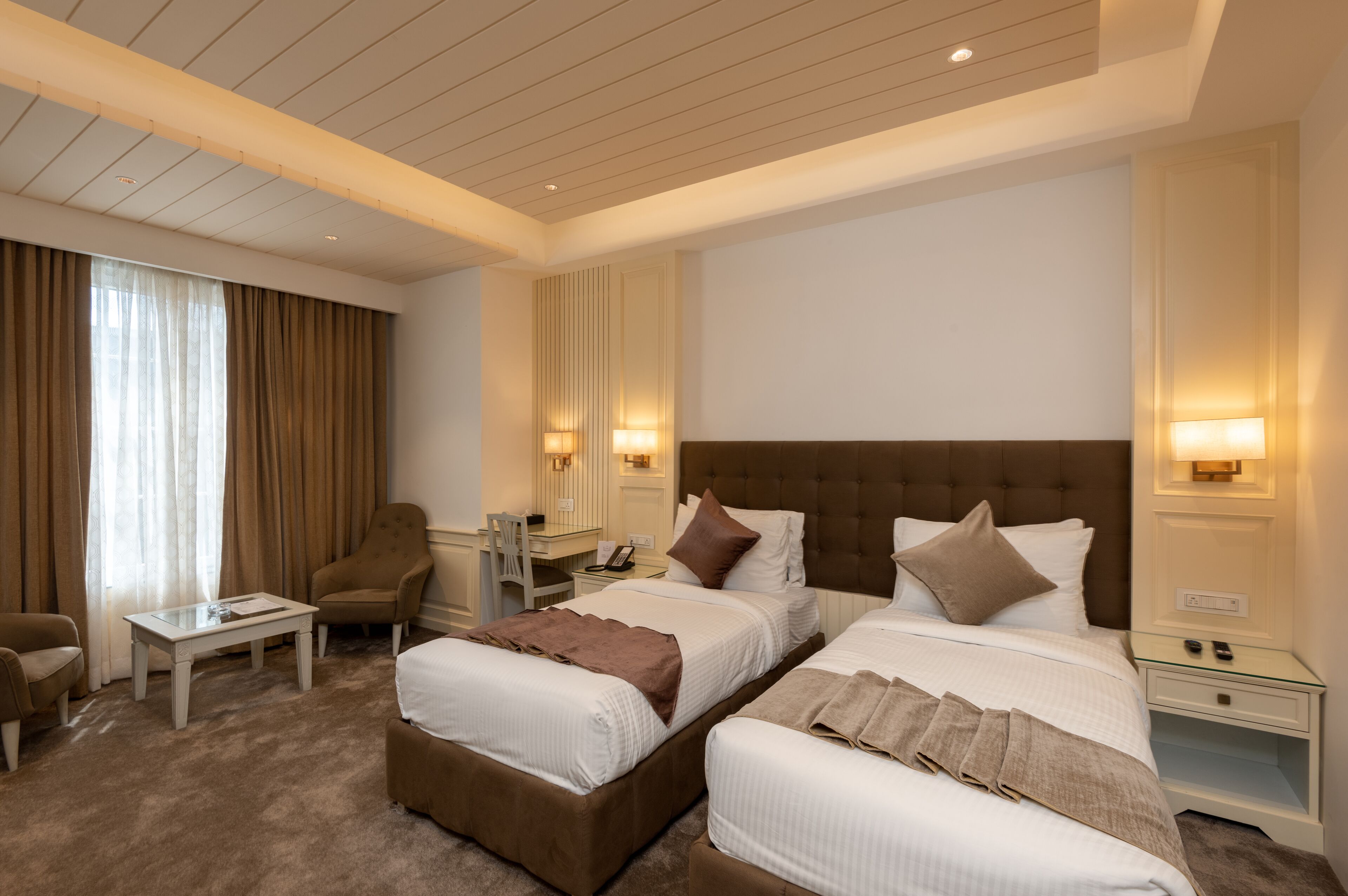 A hotel room with two beds, a desk, a chair, and a small table.
