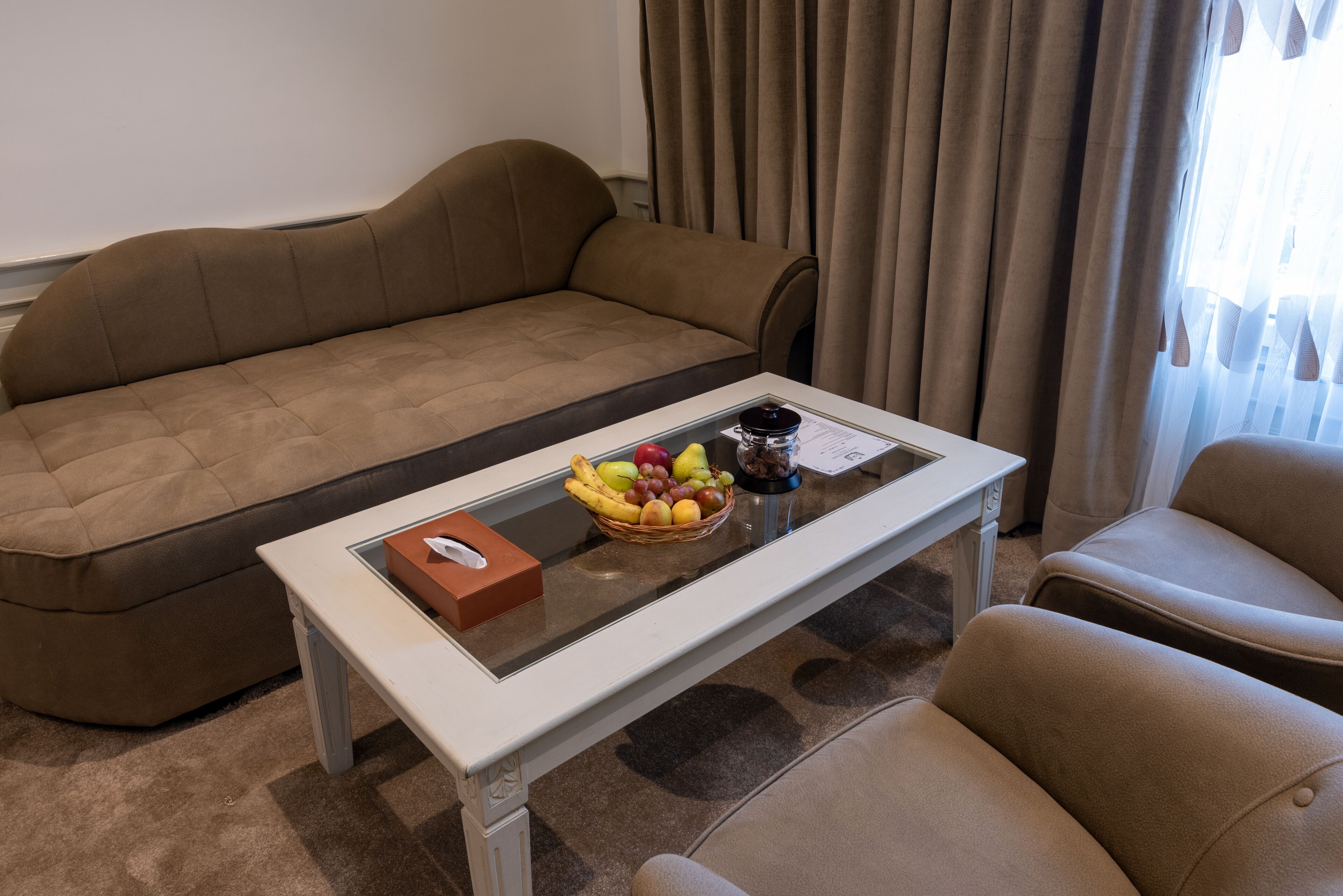 A modern living room with a beige sofa, a glass-top coffee table with a fruit basket, and a white side table.
