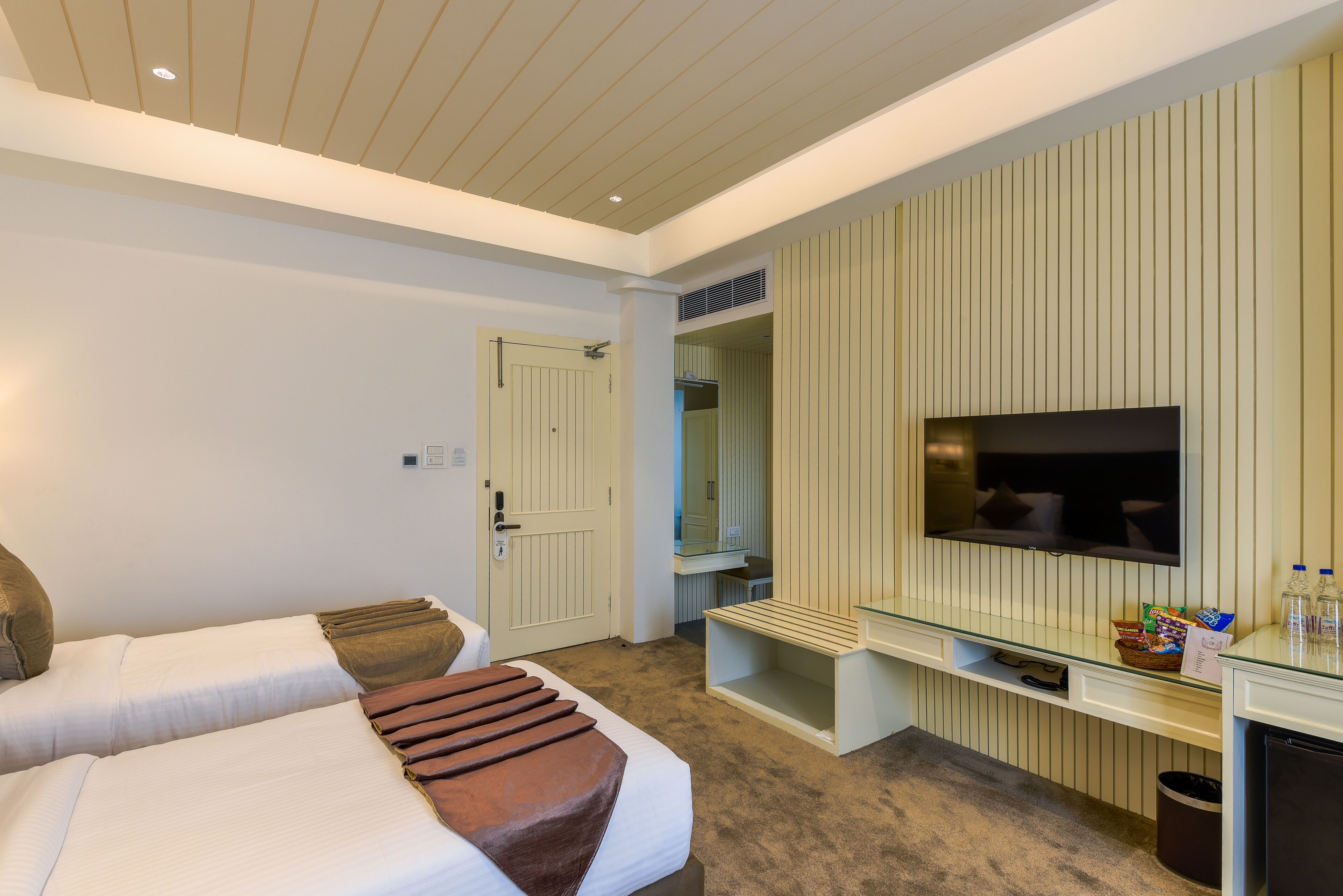 A hotel room with two beds, a television, a mirror, and a small desk with a TV stand.