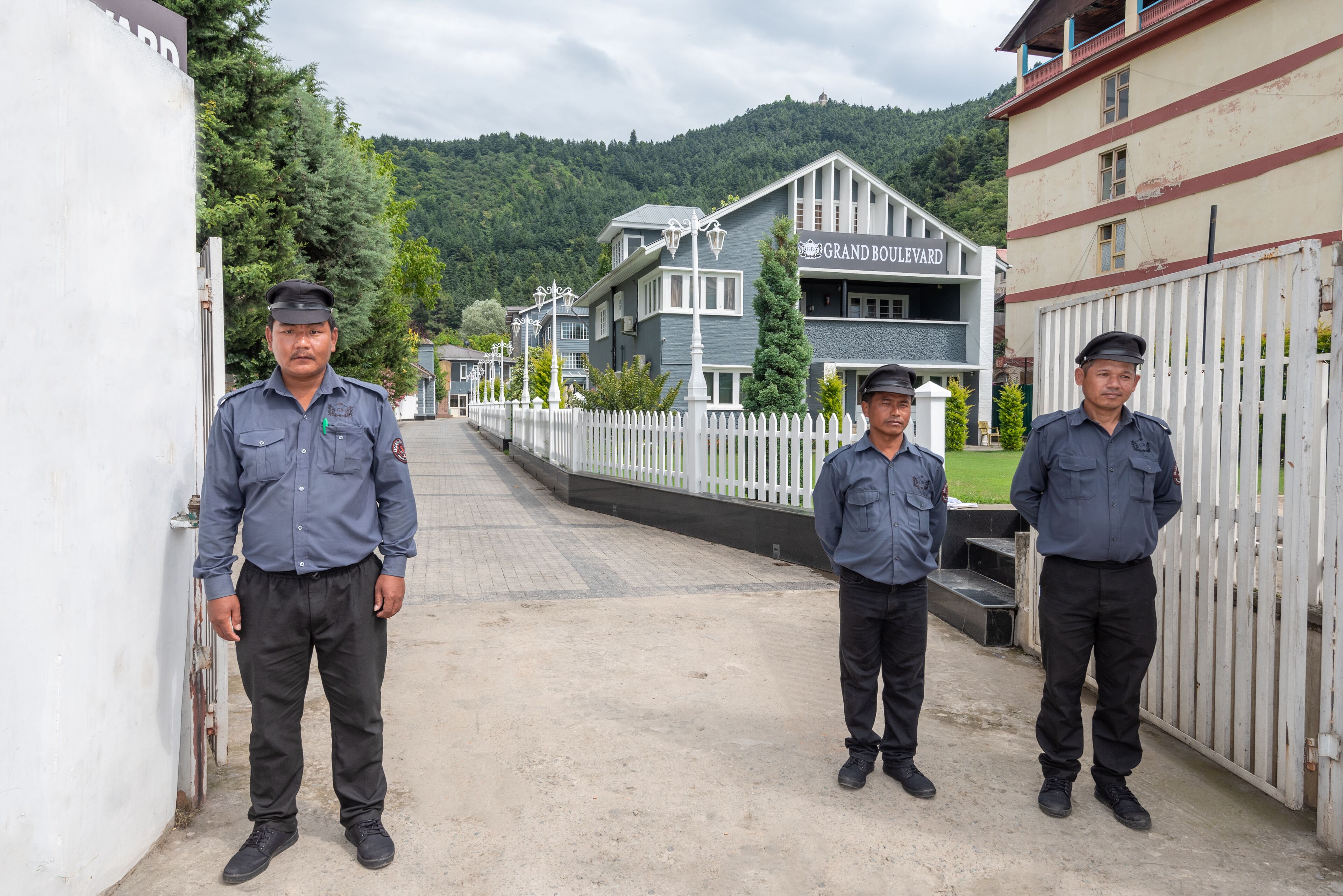 A gated entrance with a white picket fence, a building labeled "Grand Boulevard," and a mountainous backdrop.