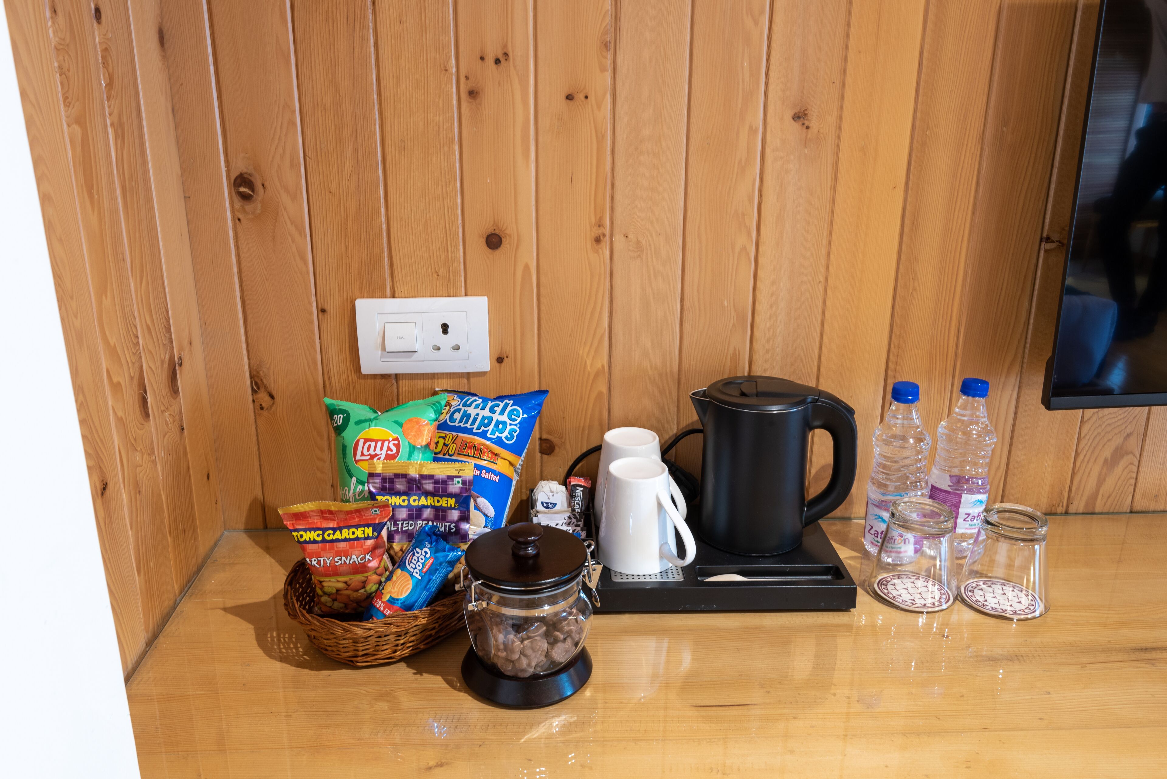 A kitchen counter with a coffee maker, a kettle, a basket of snacks, and a jar of coffee beans.