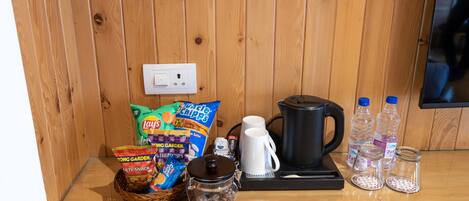 A kitchen counter with a coffee maker, a kettle, a basket of snacks, and a jar of coffee beans.