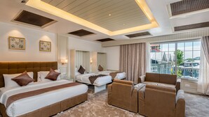A hotel room with two beds, a sofa, a large window with a view, and a ceiling with recessed lighting. - Hotel Grand Boulevard (Srinagar)
