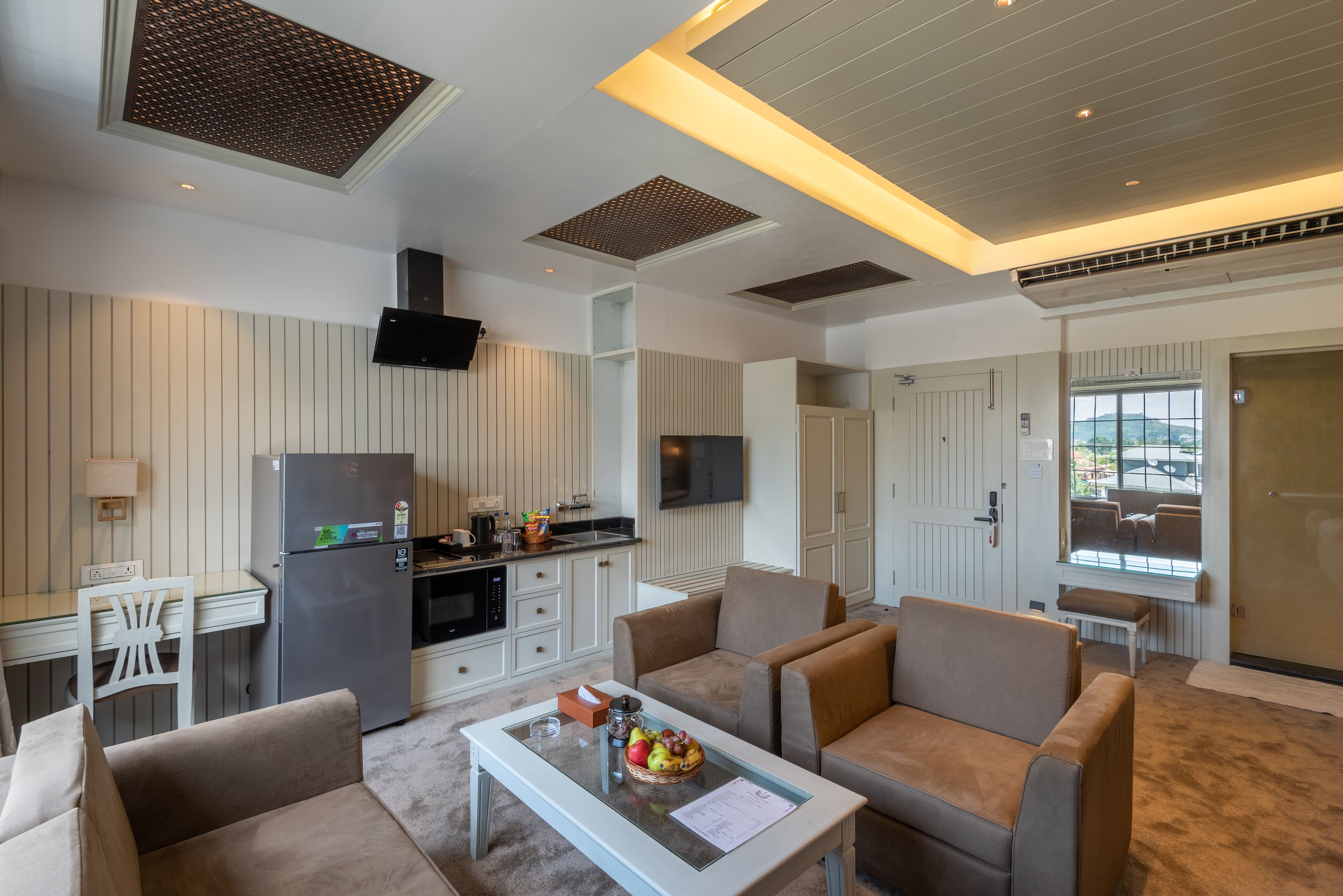 A modern living room with a kitchen area, including a dining table, sofa, and a refrigerator.