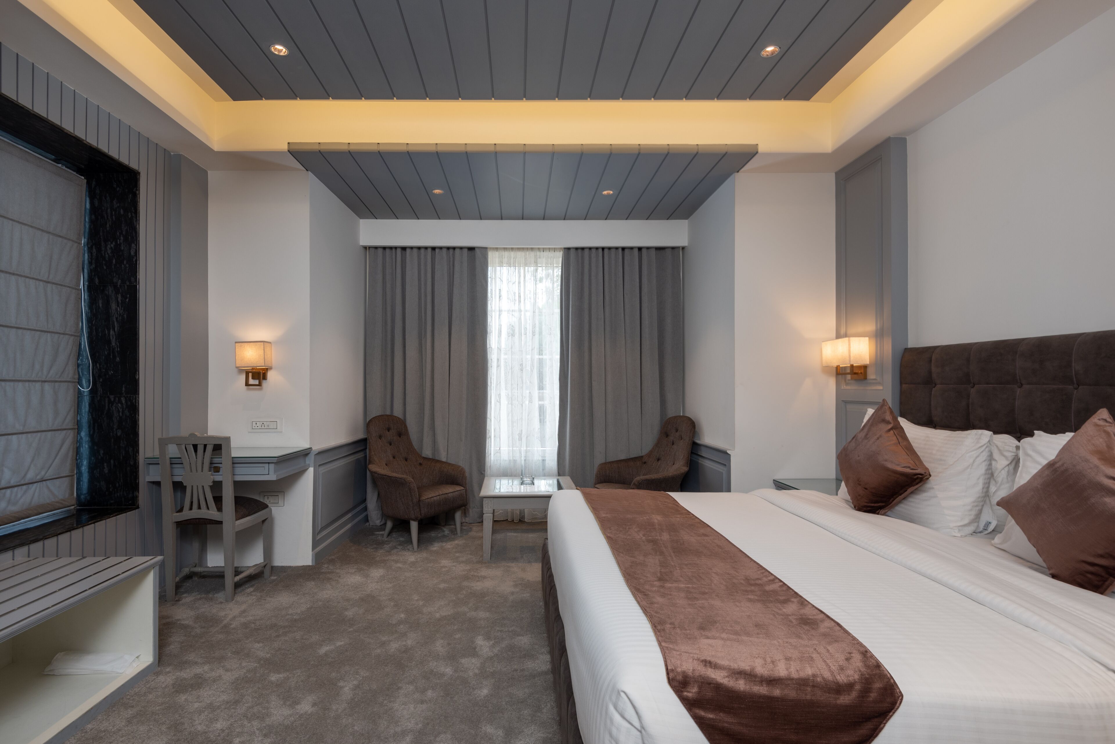 A modern hotel room with a large bed, two armchairs, a small table, and a TV.
