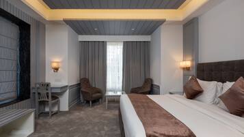 A modern hotel room with a large bed, two armchairs, a small table, and a TV.