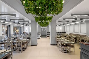 A modern dining area with multiple tables and chairs, a central aisle, and hanging greenery. - Hotel Grand Boulevard (Srinagar)