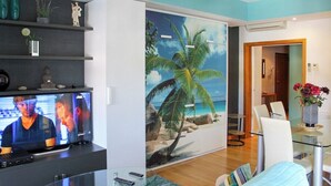 Una sala de estar moderna con una televisión de pantalla plana, una mesa de centro de vidrio y un comedor con una mesa y sillas de vidrio.
