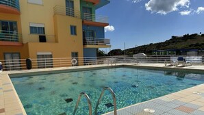 Una piscina con agua cristalina, rodeada por una solana con baldosas y un edificio con balcones.