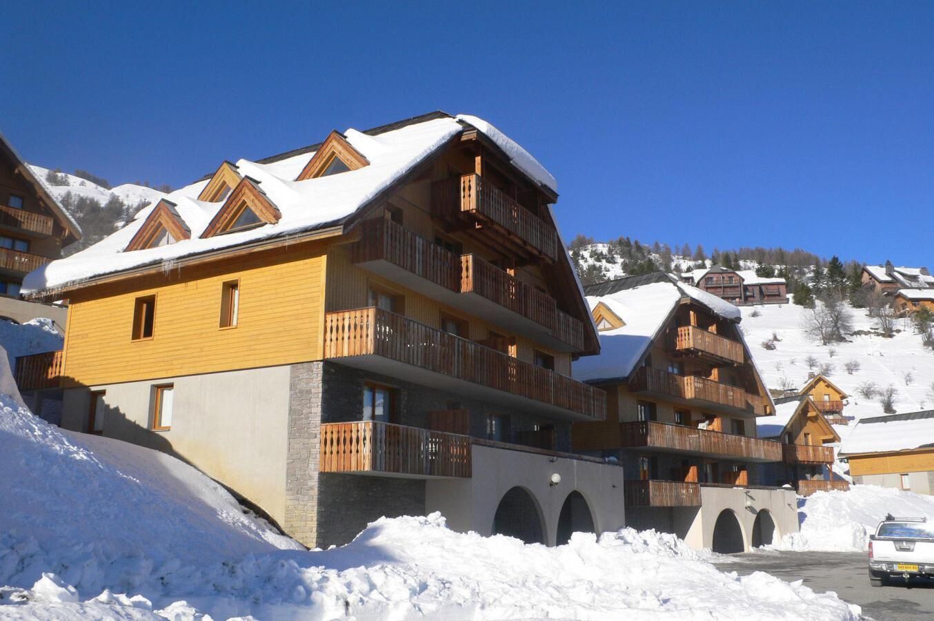 A multi-story chalet with balconies, set against a snowy mountain backdrop.