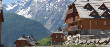 A mountain lodge with multiple wooden buildings, a stone wall, and a view of snow-capped mountains.