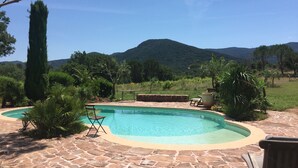 A swimming pool with a stone patio, surrounded by greenery and a mountain in the background. - Two little romantic cottages in the middle of nature  (Les Mayons)