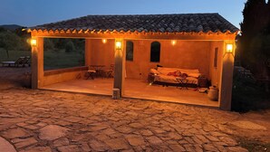A cozy outdoor patio with a tiled roof, a sofa, and a table. - Two little romantic cottages in the middle of nature  (Les Mayons)