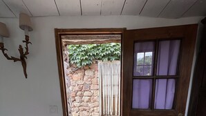 A room with a wooden door leading to a stone wall and a small garden. - Two little romantic cottages in the middle of nature  (Les Mayons)