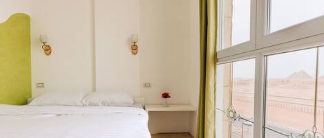 Ein Hotelzimmer mit großem Fenster, einem Bett, einem Nachttisch und Blick auf die Wüste.