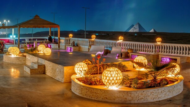 A rooftop terrace with seating areas, decorative lighting, and a view of the pyramids. - Desert Moon (Giza)