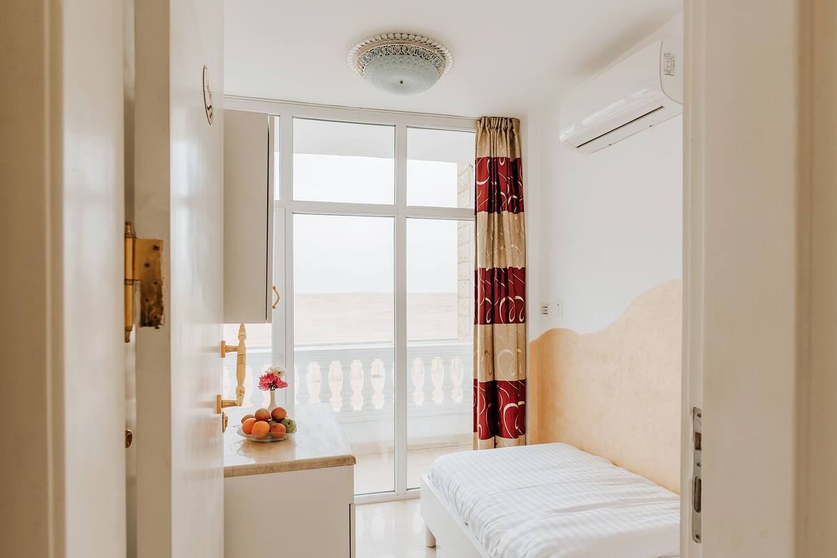 Ein Schlafzimmer mit Bett, einem Fenster mit Vorhängen, einer Deckenleuchte und einer Wandklimaanlage.