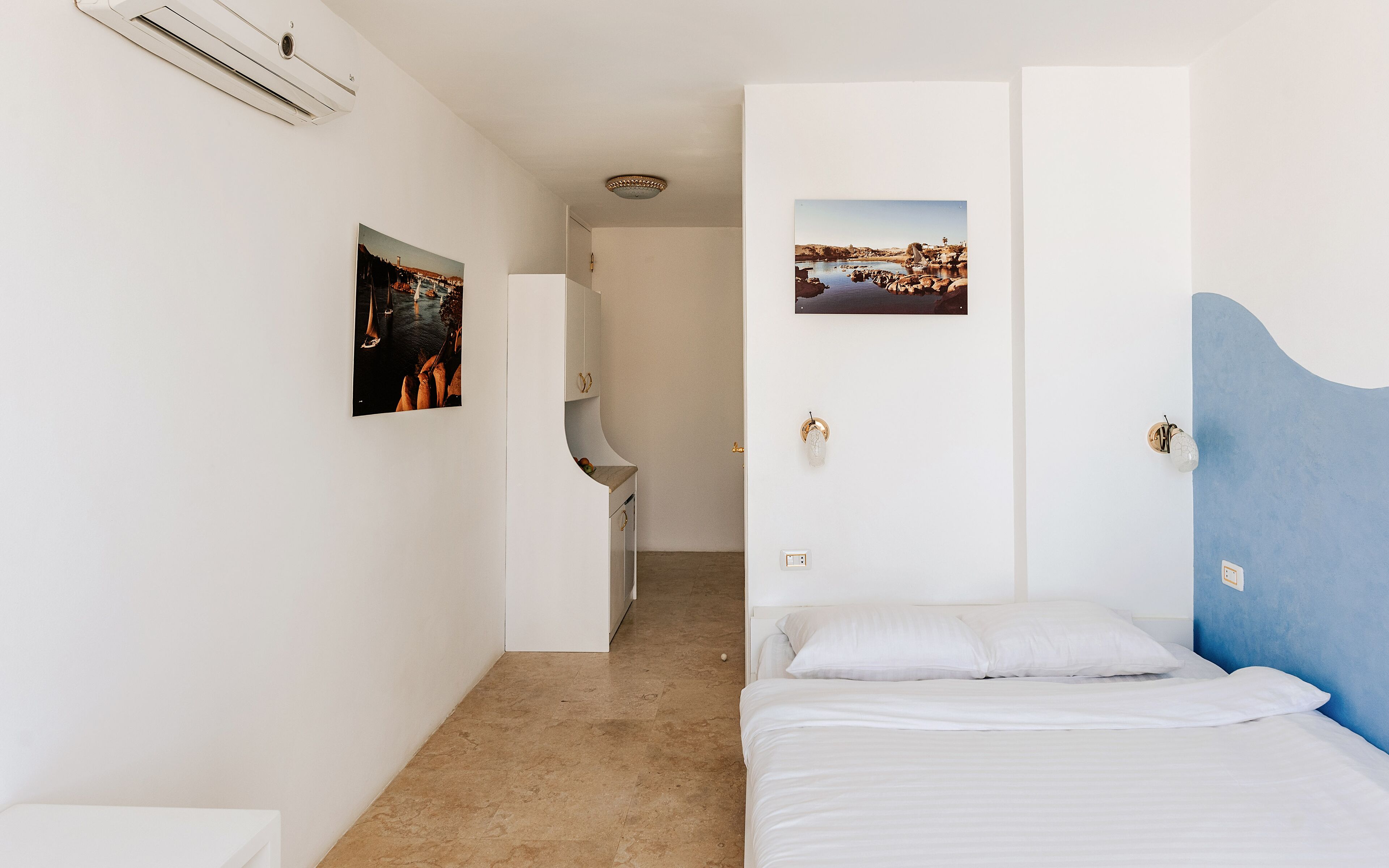 Een slaapkamer met een bed, een badkamer met een wastafel en twee afbeeldingen in lijsten aan de muur.