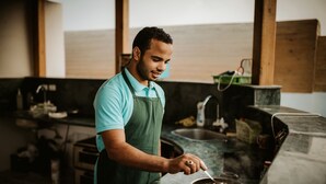 A person cooking in a modern kitchen with a large window, a sink, and a countertop. - Desert Moon (Giza)