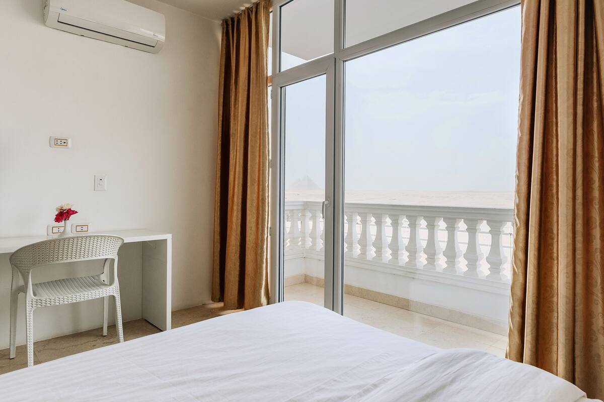 Ein Hotelzimmer mit Bett, Schreibtisch, Stuhl und einem großen Fenster mit Vorhängen.