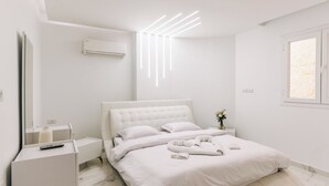 A modern bedroom with a white bed, a bedside table, a nightstand, and a wall-mounted air conditioner. - Desert Moon (Giza)