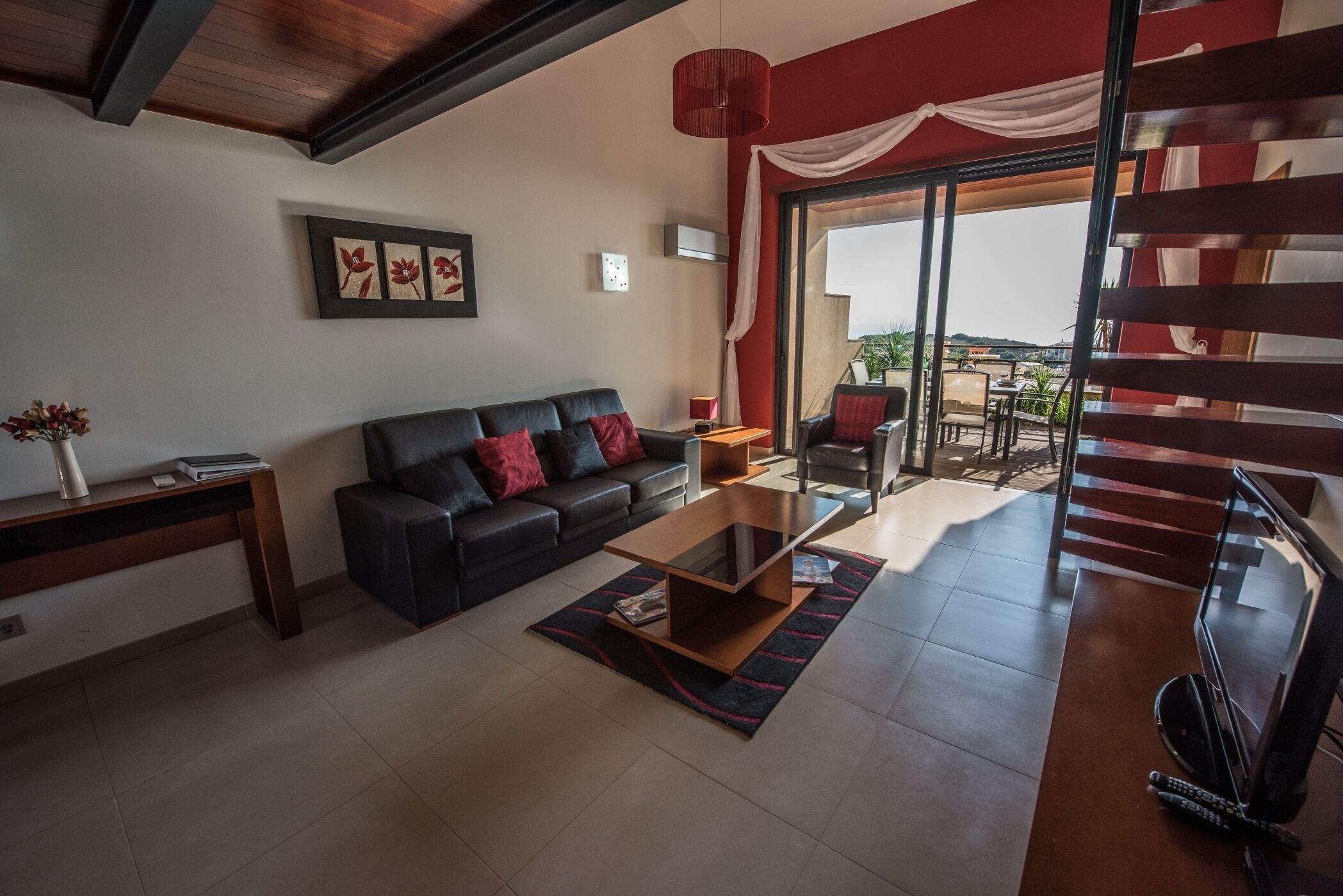 Uma sala de estar moderna com um sofá de couro preto, uma mesa de centro de vidro e vista para o exterior por uma porta de correr.