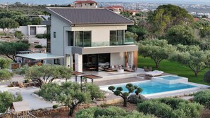 Una casa moderna de dos pisos con piscina, mobiliario exterior y vistas al paisaje circundante.