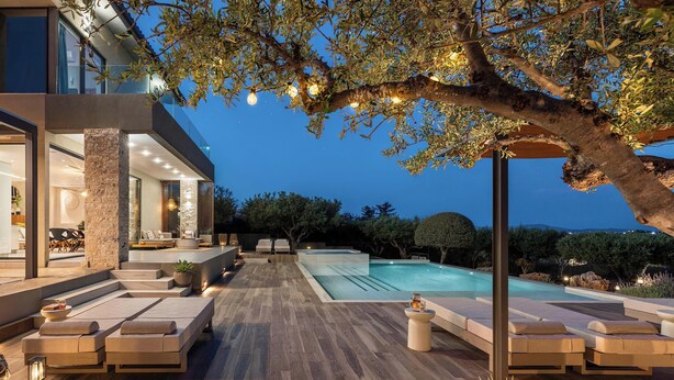 Un área de piscina moderna al aire libre con sillones de descanso y un pilar de piedra.