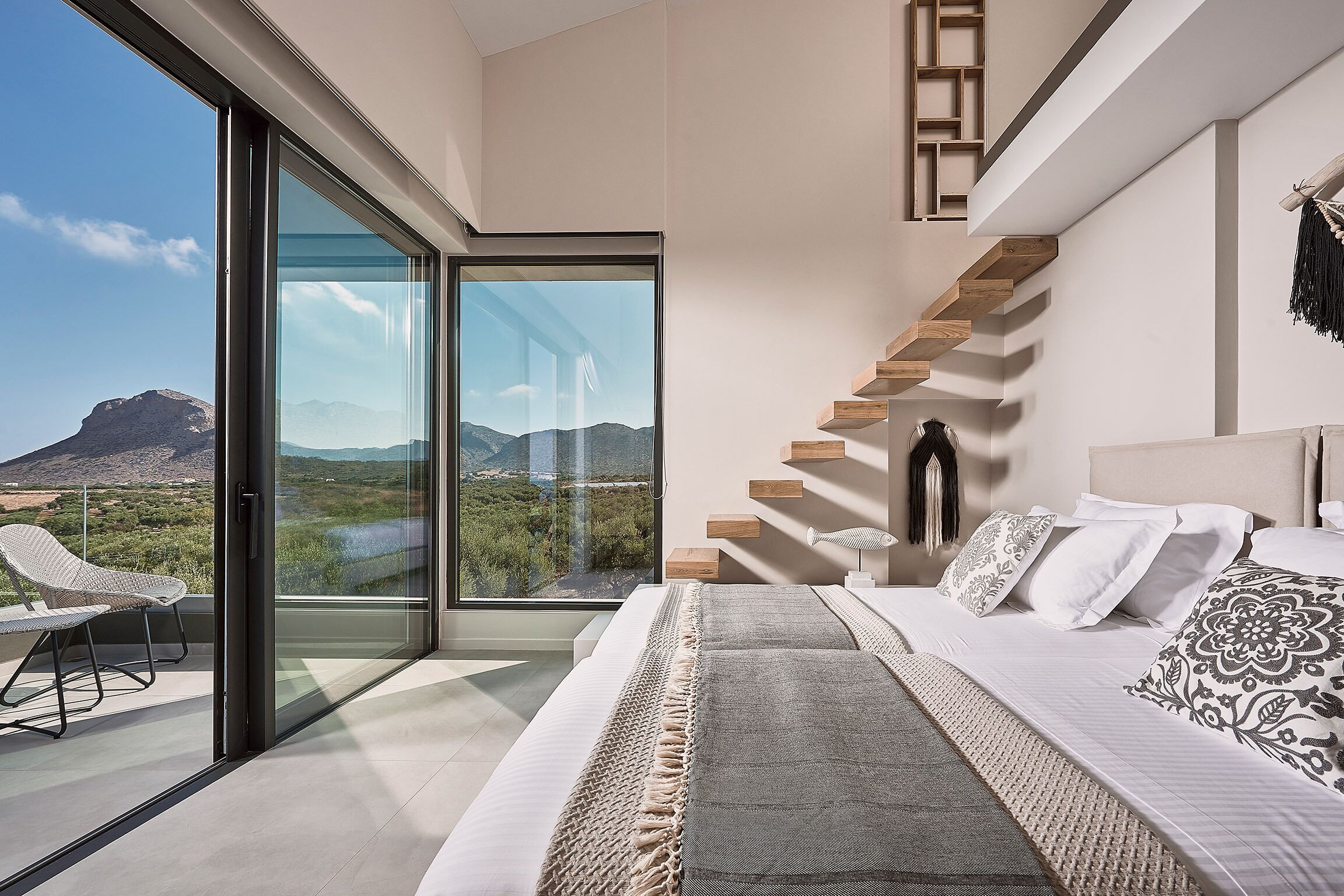 Un dormitorio moderno con una cama grande, un vidrio que da a un balcón y una escalera de madera.