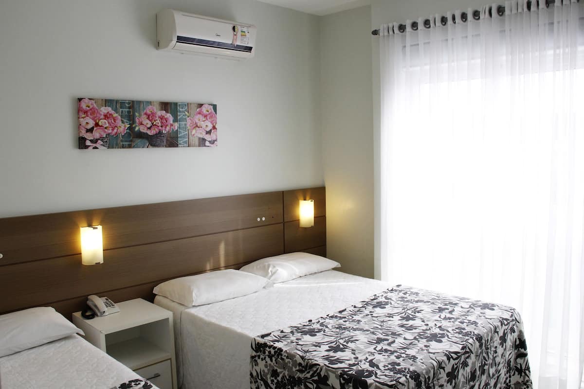 Ett hotellrum med en säng, två sängbord, en telefon som sitter fast på väggen och ett konstverk med blommotiv.