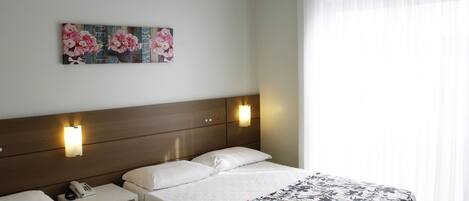 A hotel room with a bed, bedside tables, a telephone, and a wall-mounted air conditioner.