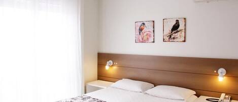 Ein Hotelzimmer mit einem Bett, zwei Wandleuchten, einem Telefon auf einem Nachttisch und zwei gerahmten Bildern an der Wand.