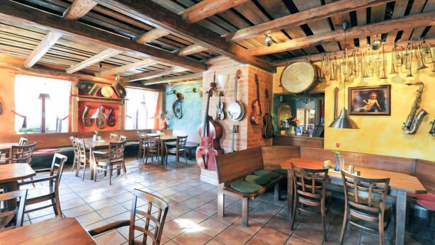 Interior rústico de un restaurante con mesas y sillas de madera, suelo de baldosas y varios instrumentos musicales en las paredes.